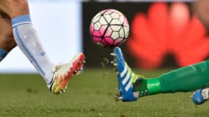 Futbol topu havadayken yere düşen bir oyuncunun ayağı ve kaleci kollarının uzandığı an.