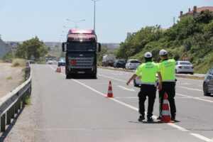 Trafik polisleri yol kontrolünde konilerle işaret verirken tehlikeli madde yüklü kamyon ilerliyor.