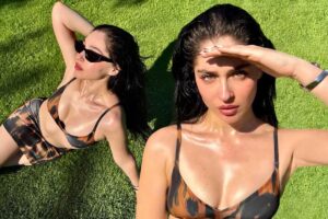 Çim zemin üzerinde siyah-bakır desenli bikini giyen iki kadın, güneş gözlüğüyle poz veriyor.