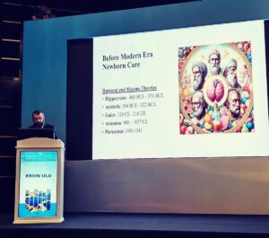 Konuşmacı kürsüde, ekranda Before Modern Era Newborn Care ve Humoral and Miasma Theories başlıkları ile görsel.