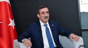 Cevdet Yılmaz, Türk bayrağı önünde koltuğa yaslanmış şekilde kamera karşısında konuşuyor.
