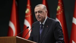 Türk bayrakları önünde kürsüde konuşan Recep Tayyip Erdoğan, iki mikrofonla birlikte.