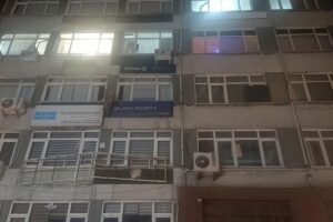 Apartman binasının dış cephesinde pencereler, elektrik kutusu ve ışıklı tabela görünüyor