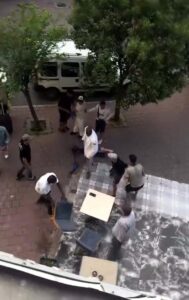 Ağaçların yanında sokakta silahlı kavgaya müdahale eden kişiler ve polis aracının görüntüsü.