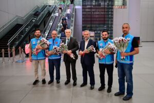 Hacılara dönüşte havaalanı girişinde çiçek buketleriyle poz veren beş kişi