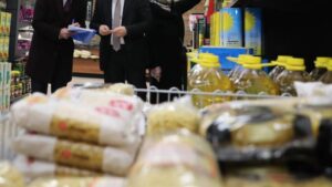 Market raflarında paketli gıda ürünleri ve kasada elinde dosya bulunan kişiler, yakın plan görüntü.