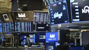Borsa ekranları ve gösterge panelleri önünde çalışan bir kişi, merkezde Citadel Securities ve Verizon yazıları görünüyor.