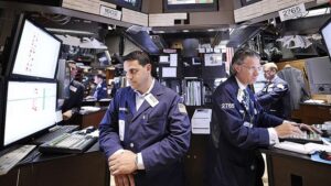 Borsa işlem katında iki çalışan bilgisayar ekranları ve klavyelerle işlem yapıyor.