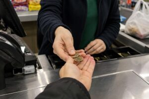 Kasada bir görevli para sayarken müşterinin elinden madeni paraları avucuna alıyor.