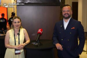 Haberler.com basın önünde iki kişi ve ortada mikrofon, erkek koyu takım elbiseyle ayakta gülümsüyor.