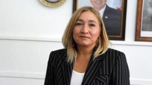 Blazer ceketli kadın, elçilik binası içinde bir koltukta otururken kameraya gülümsüyor.