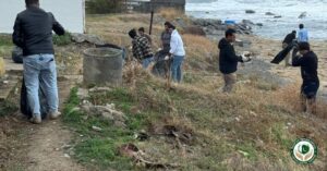 Kıyı boyunca bir grup erkek yerdeki çöpleri ve döküntüleri temizlemek için çöp topluyor.