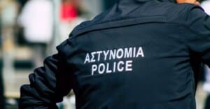 Üzerinde ΑΣΤΥΝΟΜΙΑ POLICE yazan koyu renk polis ceketi ve bir el tutan personel.