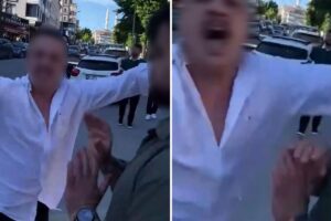 Sokakta beyaz gömlekli iki kişi el kaldırarak kameraya yakın çekimde görüntüleniyor.