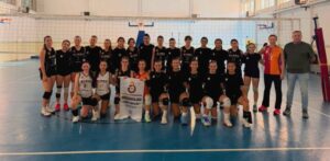 Kemal Moral Voleybol Okulu takımı, spor salonunda takım halinde kupa ve voleybol topuyla poz veriyor.