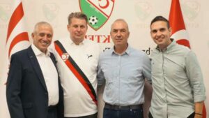 Dört erkek, arka planda Türk bayrakları ve bir duvar logosu önünde yan yana poz veriyor.