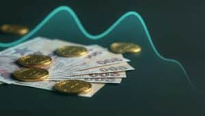 Zemin üzerinde dizilmiş euro banknotları ve altın renkli paralar, arkada dalgalı yeşil grafik çizgisiyle gösteriliyor.
