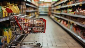 Market rafında kırmızı üst sepet ve boş alışveriş arabası, arka planda gıda ürünleri görünüyor.