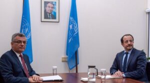 BM bayraklarının yanında iki liderin toplantı masasında oturduğu fotoğraf, önlerinde su sürahisi ve bardaklar var.