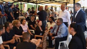Limanda ayakta ve oturarak sohbet eden kalabalık, röportaj yapan bir gazeteci ve yanında askerler ile güvenlik personeli…