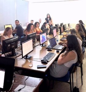 Bilgisayarlarla dolu sınıfta öğretmenler yapay zeka eğitimi alırken monitörler önünde oturuyor