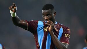Siyah forma giyen bir futbolcu kolunu havaya kaldırırken elini ağzına götürüyor, maç anında poz veriyor.